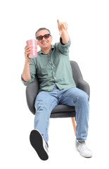 Poster - Mature man with 3D glasses and popcorn in armchair pointing at something on white background