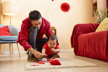 Full Length Portrait Of Happy Asian Father Playing With Cute Baby Boy Sitting On Floor At Home And Hanging Red Paper Decorations For Chinese New Year Celebration, Copy Space