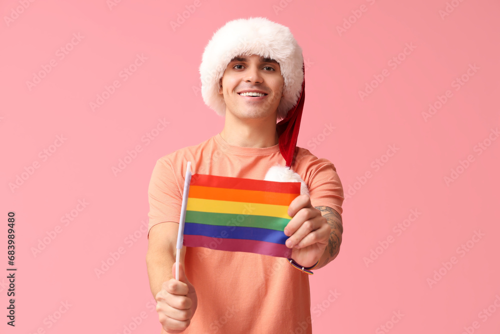 Young man in Santa hat with LGBT flag on pink background