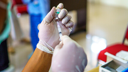 photo of a doctor with his left hand holding a vaccine and a syringe on his right measuring the dose of tetanus vaccine before injecting a patient with elementary school age children