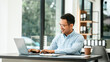 © NanSan - Middle-age Asian businessman smiles while looking at a laptop, possibly working as a Market Researcher or Marketing Analyst.