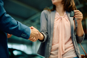 Wall Mural - Close up of woman shaking hands with car salesman in showroom.