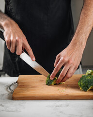 Wall Mural - Chef cutting broccoli on a wooden board preparing healthy meal