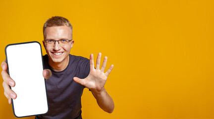 Handsome man showing five fingers and holding smartphone with empty white screen display for new Application and showing thumb up on bright yellow studio wall background. Mockup banner