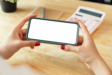 Wall Mural - Female hands holding smartphone with mockup of blank screen on desk in office.