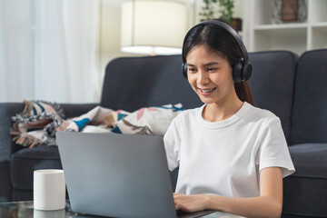 Wall Mural - Smiling Asian woman wear headphones and using laptop on desk.