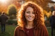 © kapros76 - Smiling young curly redhead attractive mature woman posing at a beautiful garden looking at the camera during late autumn sunset with a sun flares in the background, surrounded by friends and relative