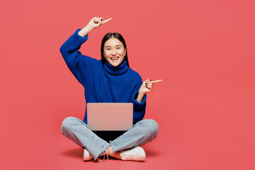 Wall Mural - Full body young IT woman of Asian ethnicity wear blue sweater casual clothes sitting work hold use laptop pc computer point aside on area isolated on plain pastel pink background. Lifestyle concept.