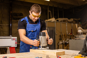 Wall Mural -  A young brunette man carpenter equals a wooden plank with a milling machine in the workshop