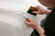 A specialist in wrapping a car with white vinyl film in the process of work. Car wrapping specialists cover the car with vinyl film.