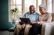 © Danny - Two happy seniors smiling while using a digital tablet in living room. Diverse senior couple sitting on sofa using tablet.