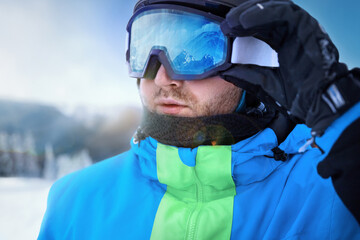 Wall Mural - Close Up Of The Ski Goggles Of A Man With The Reflection Of Snowed Mountains. Man In The Background Blue Sky.  Winter Sports.