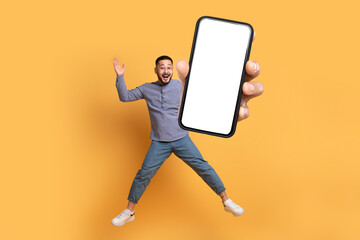 Wall Mural - Korean guy jumping showcasing huge phone with empty touchscreen, studio