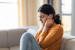 © Prostock-studio - Upset young woman sitting on couch and covering her ears with hands