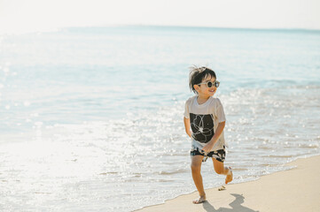 4 years boy wearing sunglasses is playing on a sandy beach near the sea.