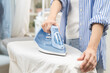 © KMPZZZ - Close up young woman hand use electric steam, hot iron press pile white shirt clothes on ironing board, housework after hygiene laundry at home. Housekeeping lifestyle, household of chores concept.