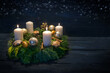 Green advent wreath with white candles, three are lit for third advent, Christmas decoration and cookies, dark blue wooden background with star bokeh, copy space