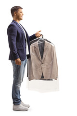 Wall Mural - Full length profile shot of a young man holding a suit on a hanger isolated on a white background