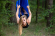 Young woman doing antigravity yoga exercises with aerial silk in the park.