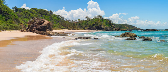 Australian coast with rocks on the seafront with a long sandy beach, view from the beach to the seaside landscape on a summer sunny day.