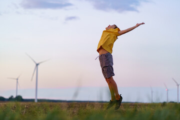 boy in yellow shirt delight leaping into air. the backdrop features silhouetted wind turbines with p
