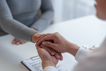 Medical service worker or doctor, pharmacist holding hands reassuring a female medical patient at a work desk in a clinic after giving advice to a female patient. Health care service concept.