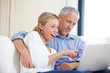 © Tabitha Rose/peopleimages.com - Mature couple, laptop and video call with conversation, smile and living room couch. Social media, technology and communication in lounge, husband and wife with connection, streaming and happy