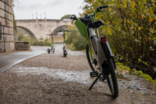 Different Electric Mobility Options In The City Of Rome. Focus On The Electric Bike, Electric Scooters In The Background. Visible Also The Aemilius Bridge. Cycle Path In Rome.