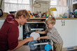 © Halfpoint - Little boy helping father to load dishwasher after breakfast. Cleaning the kitchen before leaving to work and daycare. Family morning routine.