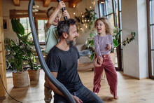 Father and kids cleaning house, vacuuming the floors with a vacuum cleaner. Young boy and girl helping with house chores.