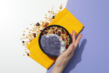 Sticker - Bowl with smoothie on towel and hand on white and purple background, top view