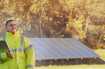 Engineer of solar energy and photovoltaic technology uses a tablet to test the service and electricity of solar panels on a sunlit field, wearing uniform as a worker of green power  and sustainability