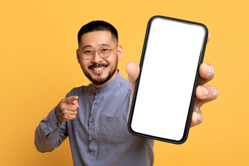 Wall Mural - Korean man with large blank cellphone pointing to camera, studio