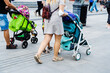 A woman and a man with baby strollers are walking along a busy street. Parents with young children on the footpath. Close-up. Selective focus