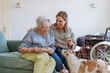 © Westend61 - Happy senior woman holding plate with healthcare worker sitting on sofa near dog at home