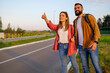 © djoronimo - Happy couple hitchhiking on roadside trying to stop car.