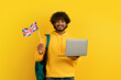 Happy young indian guy holding laptop and flag of UK