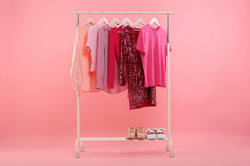Wall Mural - Rack with different stylish women`s clothes and sneakers on pink background