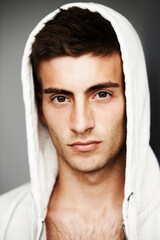 Serious, portrait and man in hoodie for fashion isolated on a gray background. Confident young person, face of model and streetwear clothes, casual and cool facial expression in Spain on a backdrop