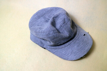 The gray cloth hat is in a worn condition with several tears. Cream background