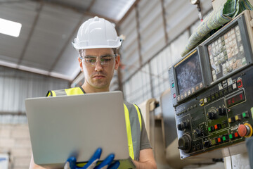 Male engineer using laptop examining with control panel CNC machine at factory. Woman technician in vest and helmet safety working at workshop heavy metal industrial.