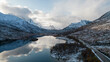 Aerial photo of a calm Norwegian mountain alpine lake in the Winter in the Arctic Circle of Norway.  Cloudy skies with snowcapped mountains.  Shot on a drone