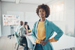 © Flamingo Images - Smiling young businesswoman standing in a boardroom with colleagues meeting behind her