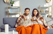 © Studio Romantic - Young couple covered in blankets sitting on sofa at home with seasonal flu or cold. Sick man and woman looking at camera and drinking hot cup of tea beverage feeling unhealthy with influenza.