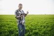 © Serhii - A young farmer inspects the quality of wheat sprouts in the field. The concept of agriculture.