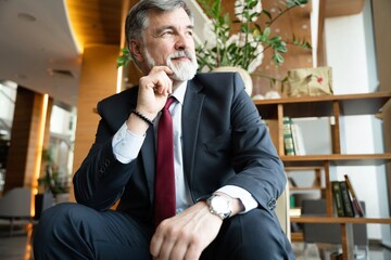 Wall Mural - Business portrait - mature businessman sitting in office lobby. Male executive relaxing in office lounge