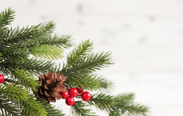 Wall Mural - Christmas fir branch with decor and pine cone on a light wooden background, copy space. Place for text. Artificial spruce branch. Selective focus