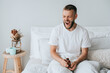 Sleepy young caucasian man in bed yawns holds jar with seeping pills, feels fatigue, needs healthy sleep. Pharmacology, medicine, recovery. Mockup, mental balance.