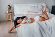 Young attractive brunette woman in elegant lingerie laying on bed being in playful mood. Hispanic model posing at bedroom. Gorgeous female with great body shape relaxing on weekend.