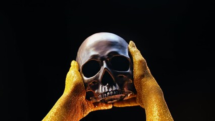 Wall Mural - Bronze scary human skull in golden female hands on black. Gothic aesthetics.